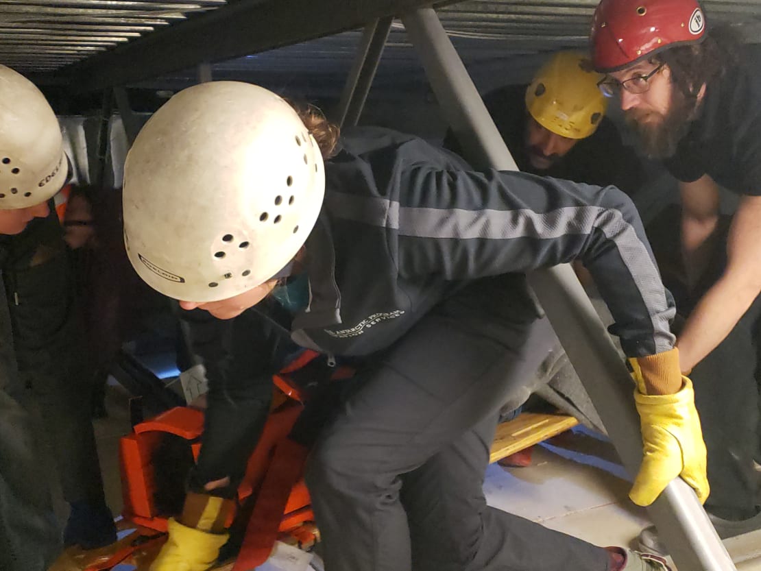 Close-up of emergency response team members in hard hats maneuvering a rescue board through a tight space.