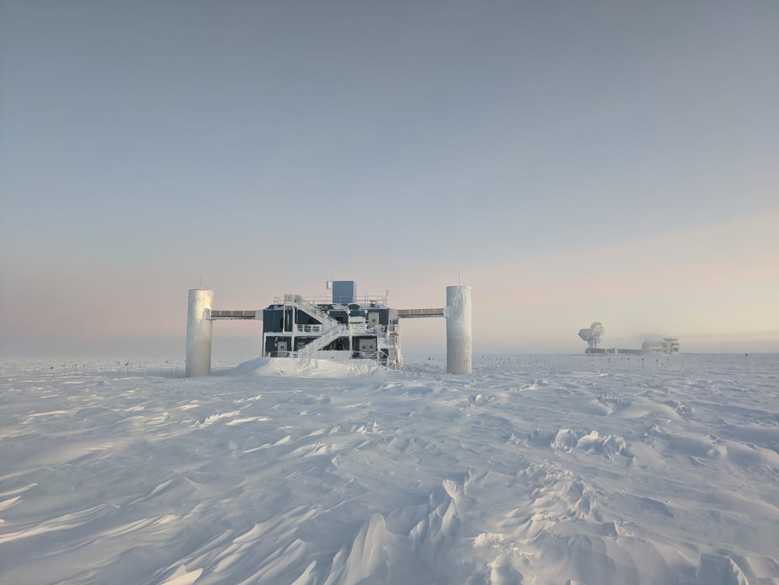 The IceCube Lab at sunrise, with South Pole Telescope visible in distance.