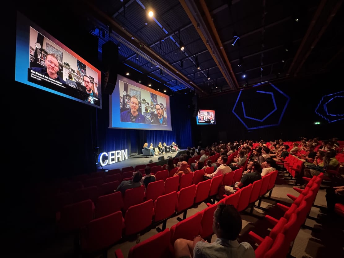 A group of people in an auditorium watching two big screens