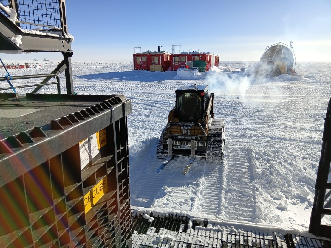 View looking down from platform toward approaching snow vehicle with forklift arms.