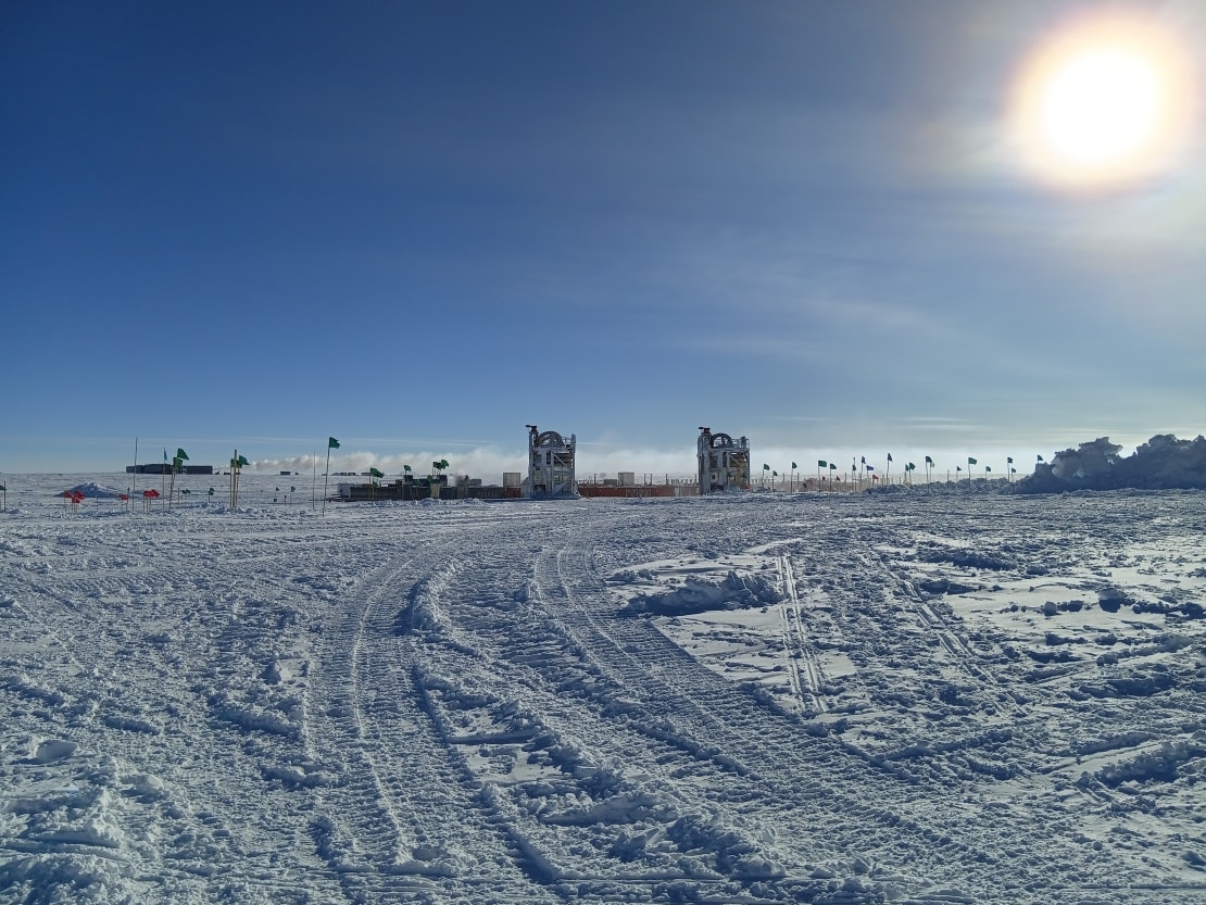 Distant view of drill camp, centered on two separated drill towers, under sunny sky.