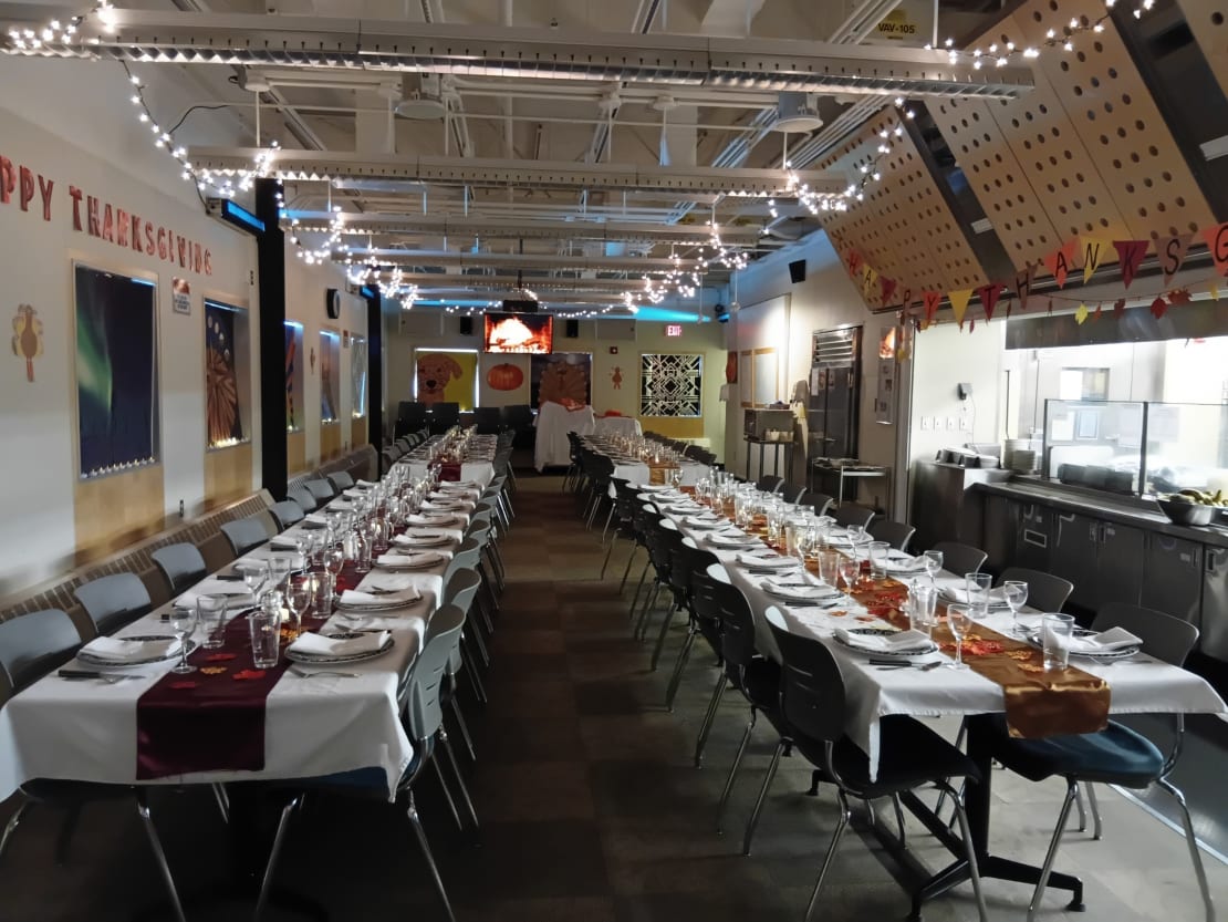 Side view of two long tables set with tablecloths and finery for Thanksgiving meal (no people).