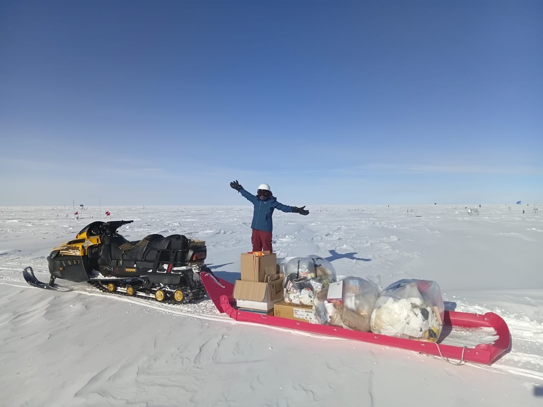 Person with arms up, standing on top of bundles of trash piled on long sled.