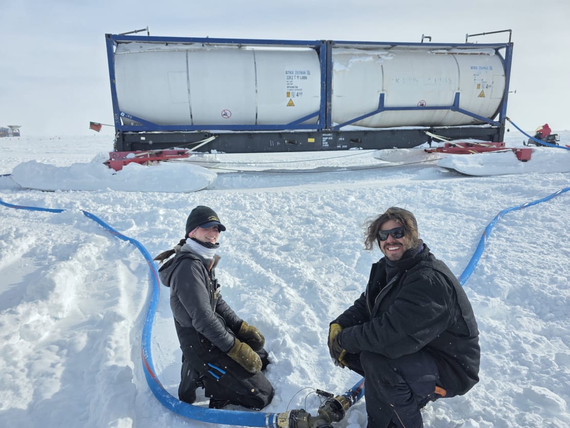 Two people facing camera as they connect water hoses out on the ice.