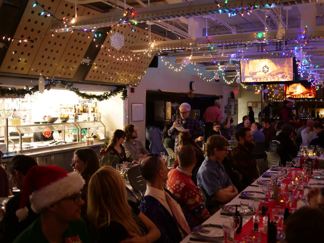View of people seated a long dinner table, with lights and festive decorations.