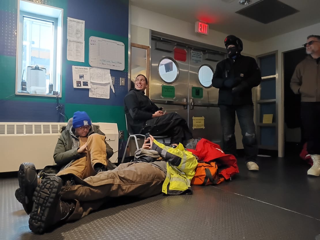 Personnel standing, sitting, and lying on the ground, waiting for flights departing the South Pole.