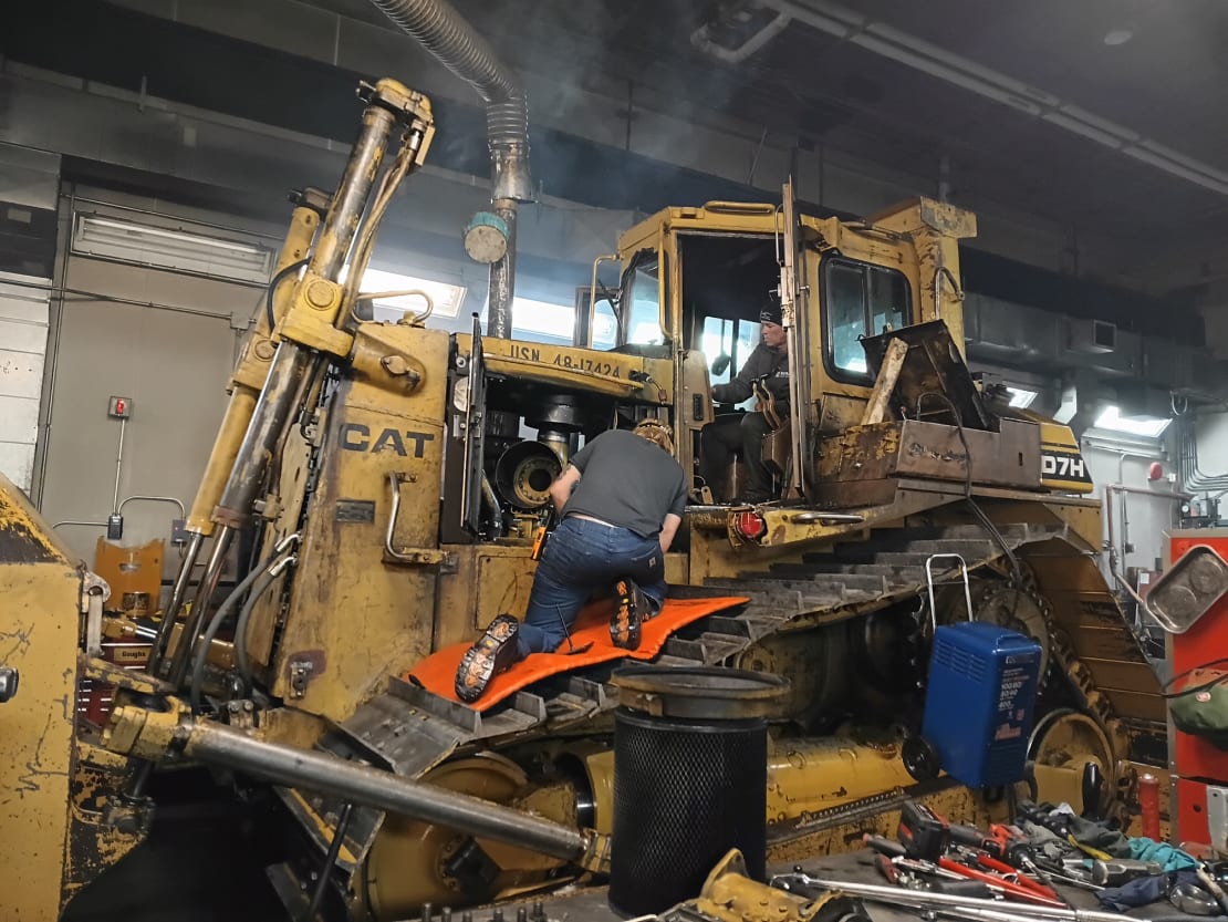 Large snow vehicle being attended to indoors in the maintenance facility.