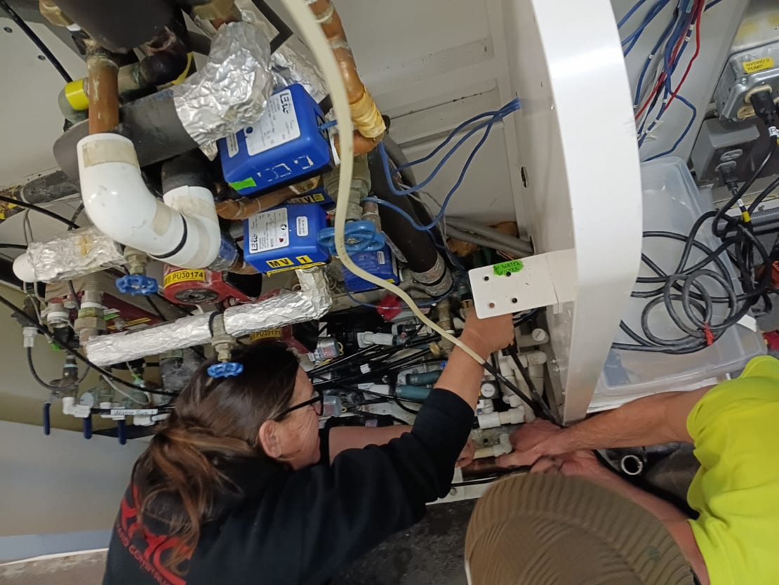 Two people crouched in repair of the water lines feeding the greenhouse.