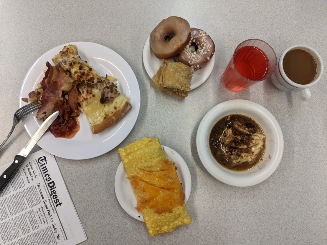 Grouping of plated breakfast items on table with utensils and newspaper.