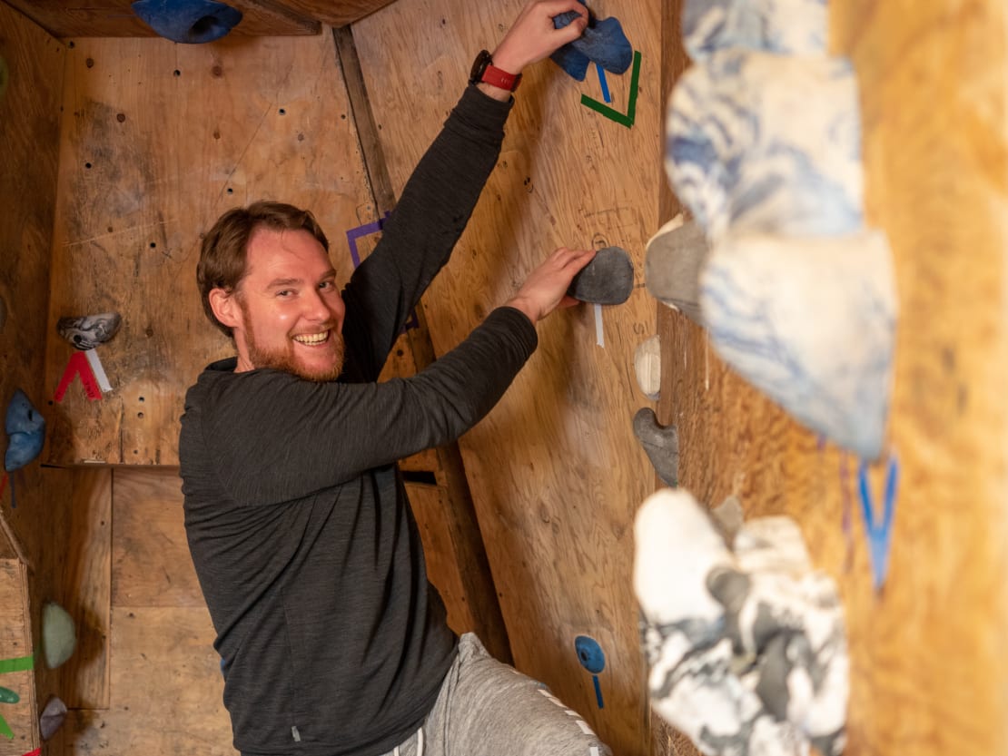 Smiling person holding onto holds of rock climbing wall.