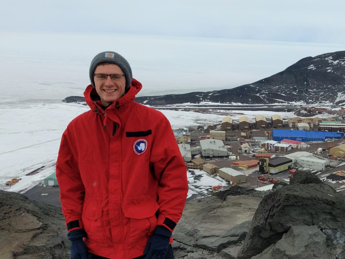 A man in a parka and beanie posing in front of a village