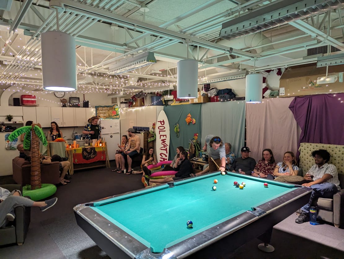 Group of people in party setting with pool table in foreground.