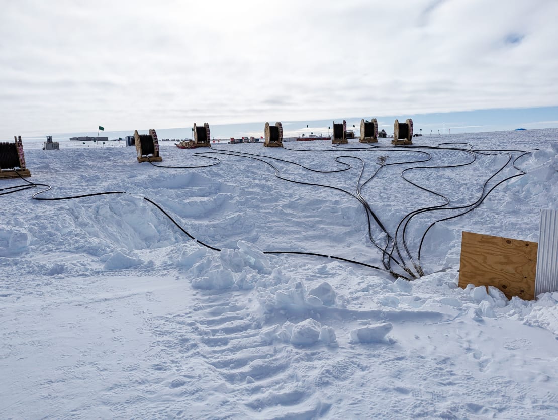 A line of large cable spools, with cable ends from each coming together on the ice where they feed into the IceCube Lab.