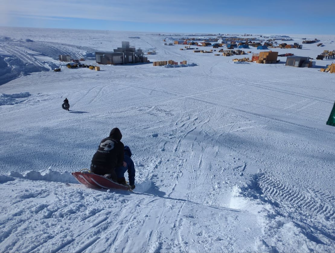 View from top of sledding hill looking down, just as a sled bearing two passengers is starting to descend.