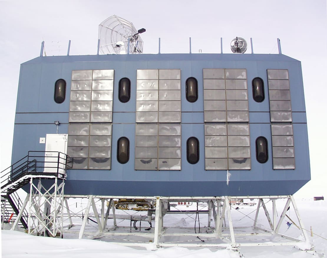 A blue, rectangular pod with 7 pill-shaped windows and a satellite dish on top. An elevated dorm at the South Pole.