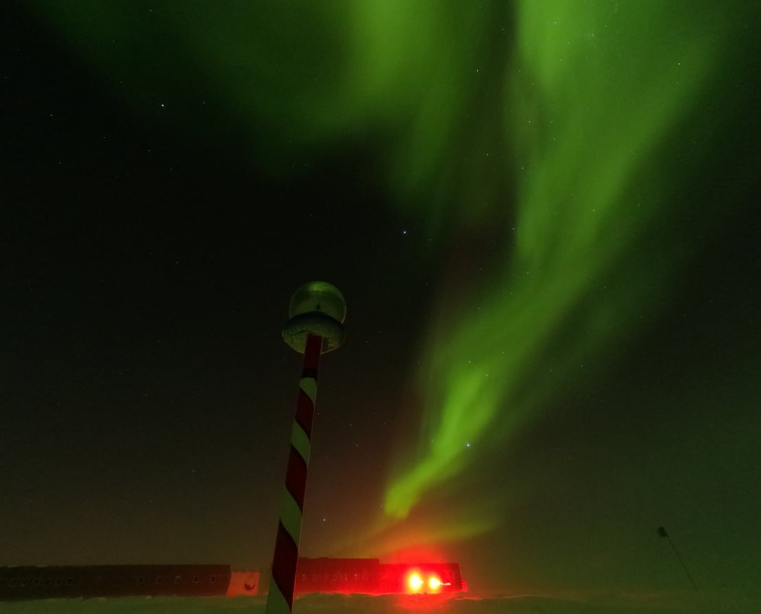 Streak of bright green aurora stretching up almost vertically in dark sky.