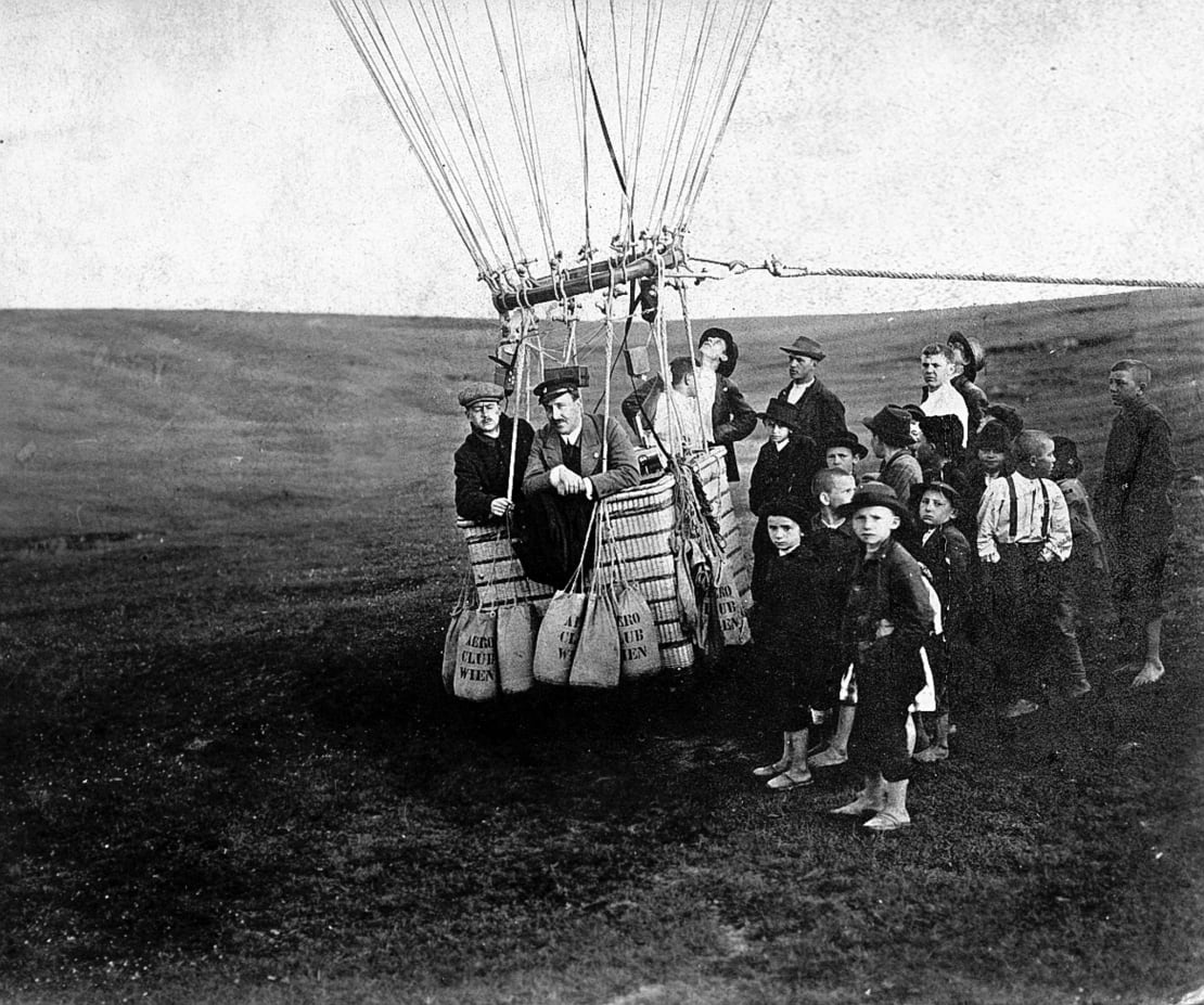 Victor Hess in a hot air balloon surrounded by onlookers.