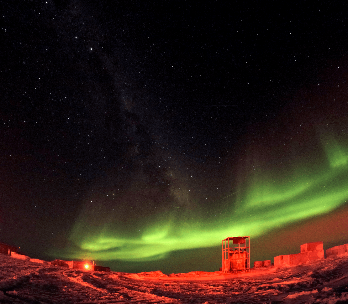 Spectacular low swath of bright green auroras above a polar landscape lit up in red.