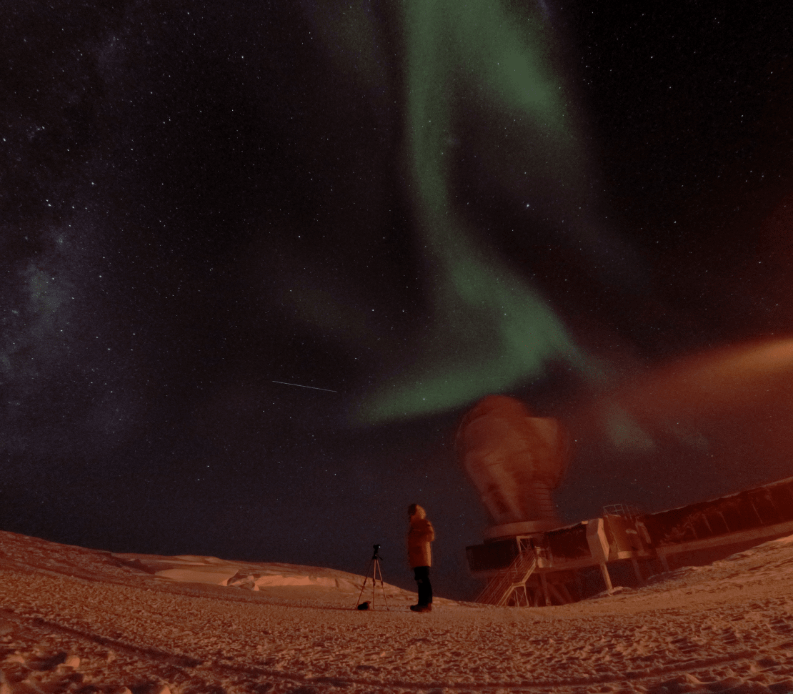A pale squiggly aurora above a person standing near the South Pole Telescope, captured a blurry image in motion.