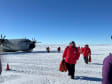 People in red parkas walking forward, away from parked plane behind them.