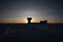 Sunrise at South Pole, with low sun directly behind South Pole Telescope, leaving surroundings in dark and shadow.