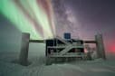 The IceCube Lab is seen with the Milky Way and auroras in the night sky at the South Pole.
