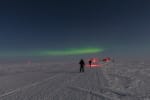 A couple of people skiing along a path at the South Pole under a starry sky.