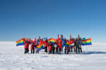 Group photo of winterovers with pride flags outside under clear sky at the South Pole.