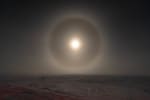 Bright moon with halo in gray sky over gray, barren landscape.