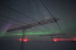 Winter skies and auroras seen through row of large antenna structures in the foreground.