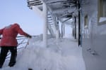 Winterover in red parka shoveling thick snow on deck of the IceCube Lab.