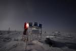 Winterover on a ladder with a lamp removing covers from a trio of field telescopes.