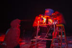 Several winterovers in middle of installing an instrument on a scaffold in the dark, under red lights.