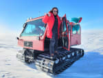 Person in red parka standing on treads of snow vehicle upon exiting.