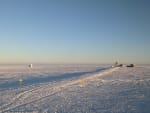 Long shadows cast on the icy surface at the South Pole from buildings in the Dark Sector, off in the distance.