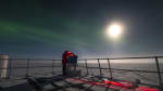 Person outdoors working on IceAct telescope, wearing red headlamp and lit from above by bright moon.