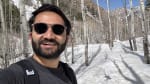 A man with sunglasses taking a selfie on a snowy hill with trees.
