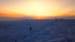The sun just starting to peek above the horizon, brightening the sky above it in shades of yellow and orange.