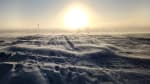 Bright sun low on horizon at the South Pole, with a few flags visible in the distance.