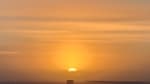 Orange sun low in sky at the South Pole, some thin horizontal clouds in the sky.