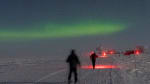 A couple of people skiing along a path at the South Pole under a starry sky.