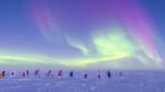 View of the ceremonial South Pole, with its circle of flags, underneath the Milky Way and a swath of auroras.