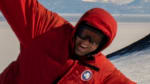 Two men in parkas posing at the South Pole