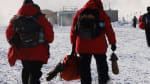 Group of people in red parkas walking out to an awaiting LC-130 plane on the South Pole skiway.