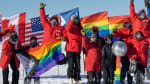 Group photo of winterovers with pride flags outside under clear sky at the South Pole.