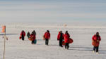 Group in red parkas walking away from plane parked on the skiway.
