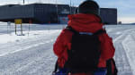 Person in red parka seen from behind on snowmobile headed toward station.