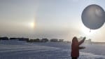 Winterover launching a weather balloon with sundog in background.