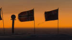 The marker and a few flags at the ceremonial Pole seen in shadow, with a bright orange sky along the horizon in background.