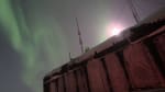 Auroras overhead and bright moon peeking over top of South Pole station.